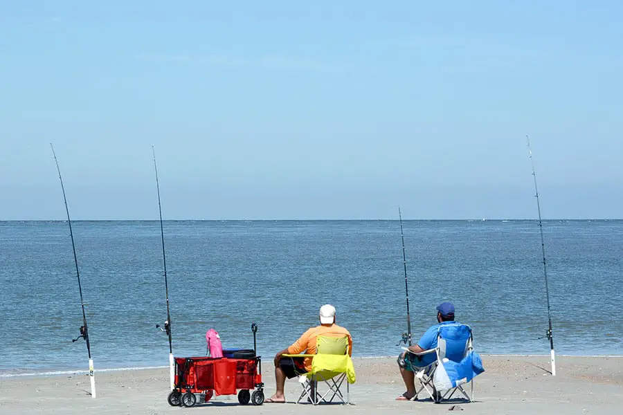 Two men sitting in chairs beach fishing