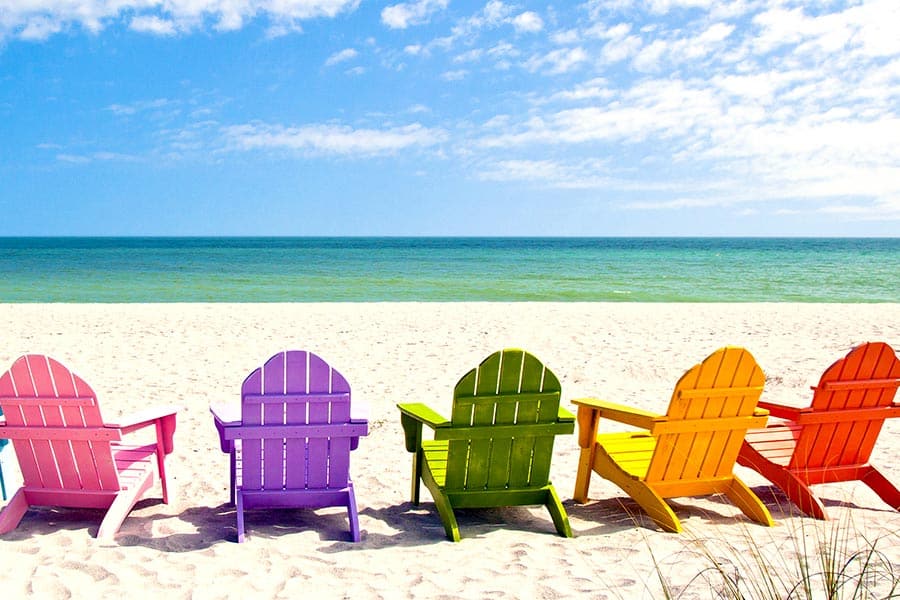 Row of colorful Adirondack chairs on beach facing the ocean