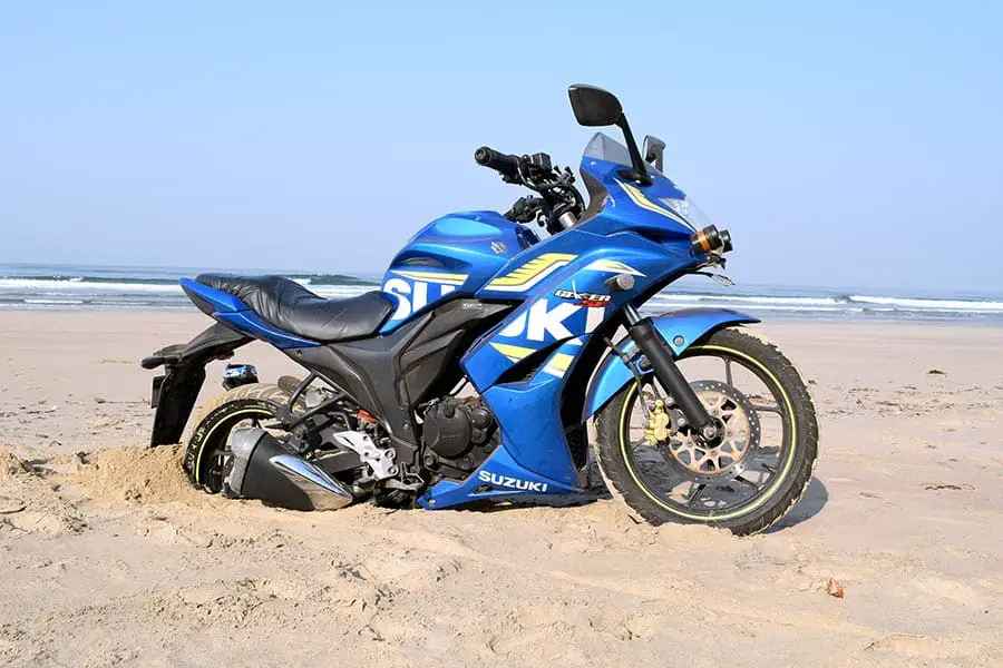 Blue Suzuki motorcycle has rear tire stuck in beach sand