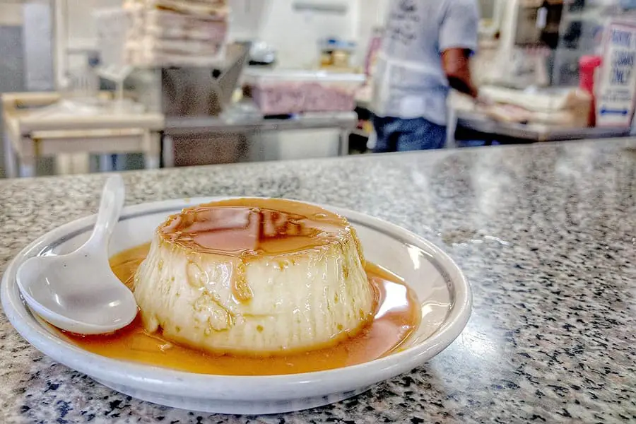 Cuban style flan on a plate with spoon sitting on counter