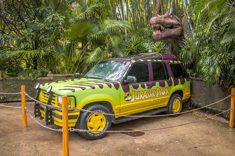 Tyrannosaurus dinosaur looking out of forest behind Jurassic Park SUV