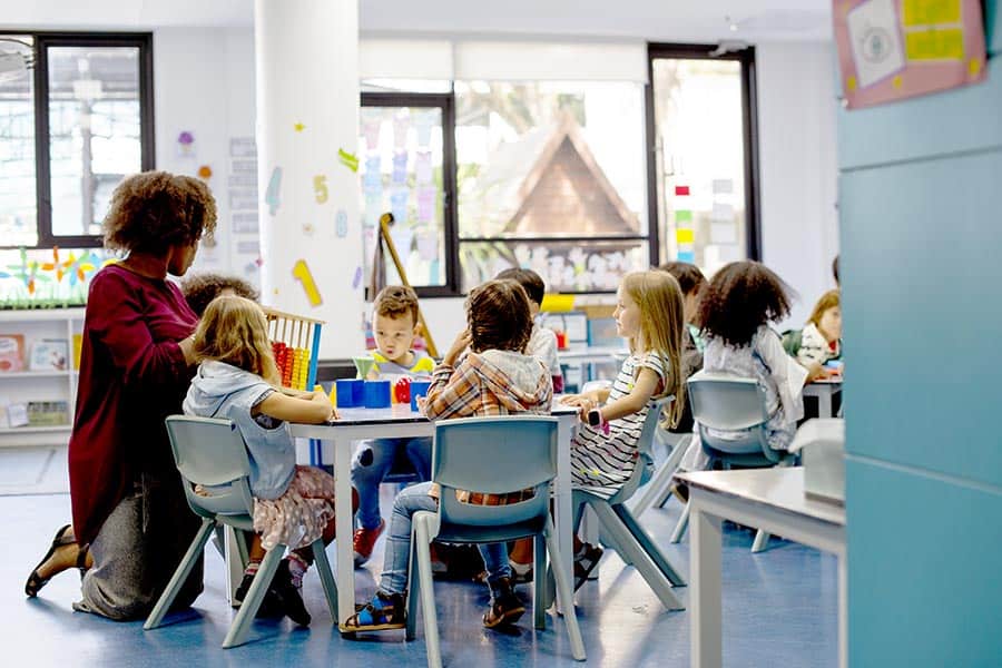 Children seated at table as daycare worker teaches them