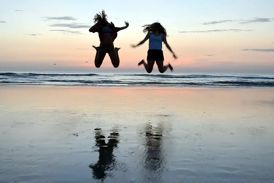 Girls jumping on sandy beach near ocean