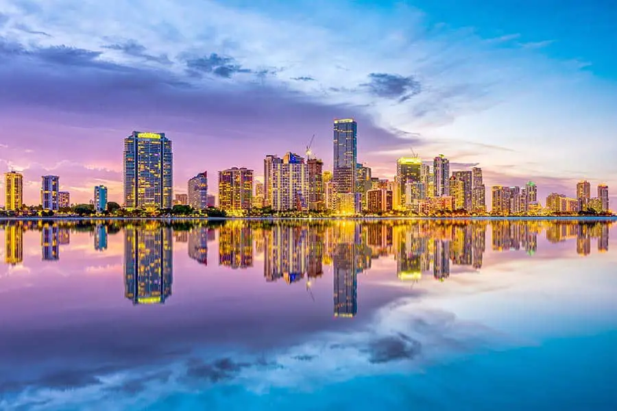 Purple clouds reflect in Biscayne Bay at dusk, city skyline on the horizon